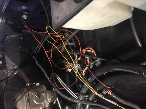 1982 Ford Bronco - A close-up view of a vehicle's engine bay, showing a tangle of red, yellow, and orange wires connected to various components. A black hose…