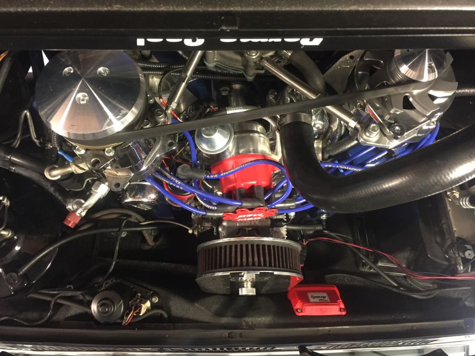 Close-up of a V8 engine bay with chrome air cleaner, red distributor, and blue spark plug wires.