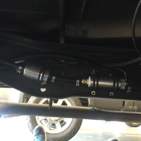 1982 Ford Bronco - The underside of a vehicle shows a fuel filter assembly mounted to the frame. The vehicle's tire and part of the suspension are visible bel…
