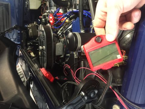 1982 Ford Bronco - A hand holds a red MSD digital ignition box over the engine bay of a blue vehicle. The engine bay contains various chrome and blue componen…