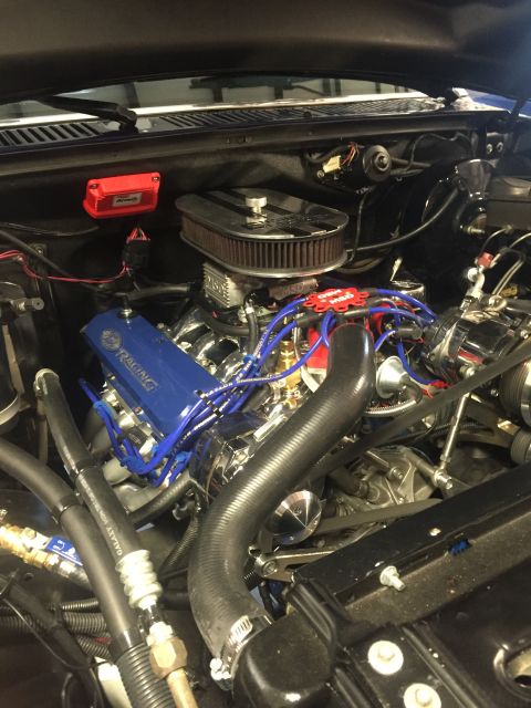 1982 Ford Bronco - A close-up view of a modified V8 engine bay, featuring a blue Ford Racing valve cover, chrome air cleaner, and bright blue spark plug wires.
