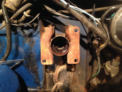 1979 Ford Bronco - This is a close-up, angled view of rusty metal brackets and a cylindrical component on a blue engine bay surface. Various wires and hoses a…