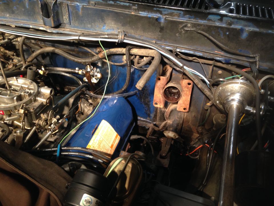 Engine bay of a vintage Ford Bronco with carburetor and hoses visible.