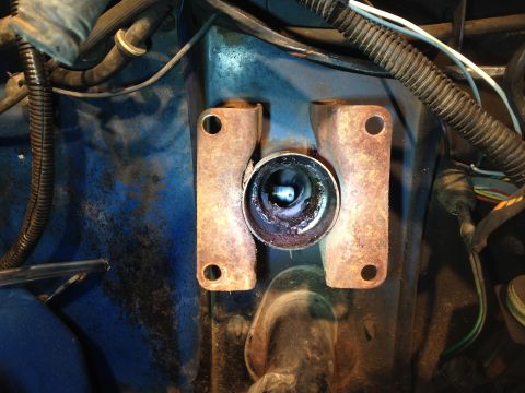 1979 Ford Bronco - A close-up view of a rusty metal bracket with a circular opening, mounted on a blue painted surface, likely in a vehicle's engine bay. Wire…