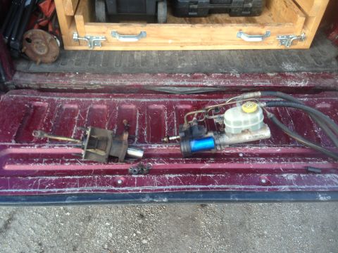 1979 Ford Bronco - A close-up view of automotive brake system components, including a master cylinder and a clutch slave cylinder, laid out in the bed of a pi…