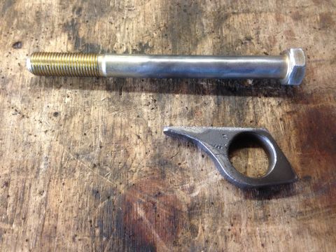 1979 Ford Bronco - A bolt and a custom metal bracket are shown on a wooden workbench, likely for a vehicle modification.
