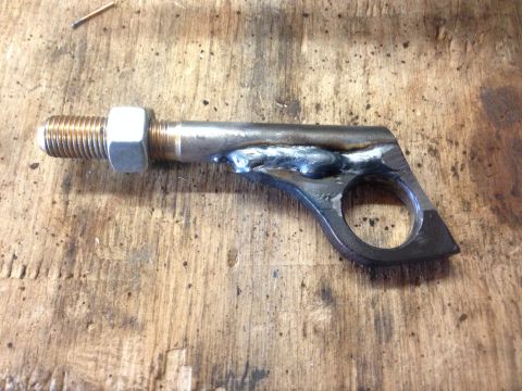 1979 Ford Bronco - A custom metal bracket with a bolt and nut assembly, welded together and resting on a wooden workbench.