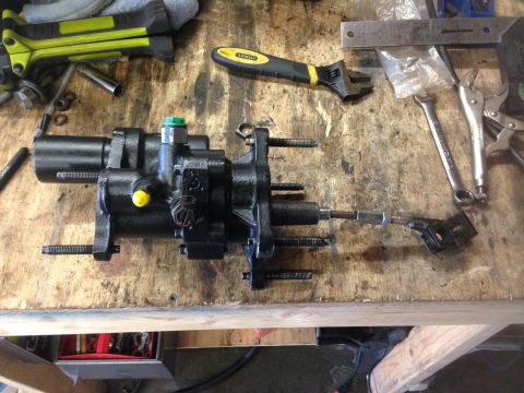1979 Ford Bronco - A hydroboost brake booster assembly sits on a wooden workbench surrounded by various tools, including wrenches and pliers.