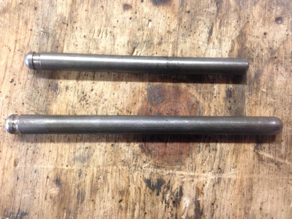 Two metal rods with rounded ends on a wooden surface. One rod is shorter than the other