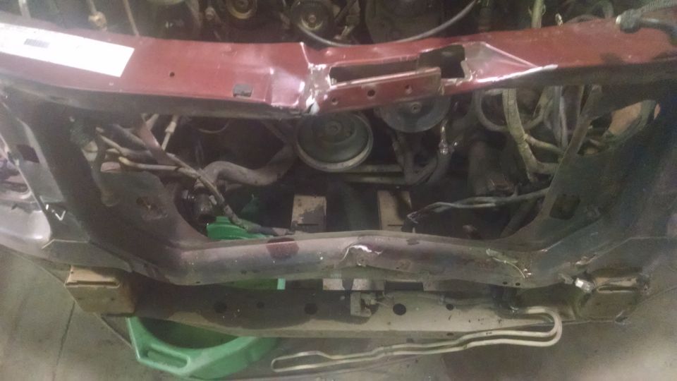Red engine bay with exposed mechanical components and wiring, supported by wooden blocks