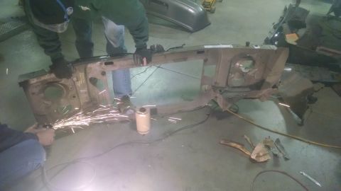 2000 Chevrolet Astro - Workers cut apart a vehicle's front end frame assembly, with sparks flying from the grinder.
