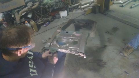 2000 Chevrolet Astro - A person uses an angle grinder on a section of vehicle frame in a workshop setting.