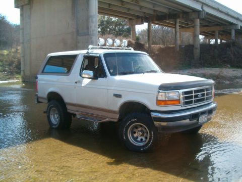 1996 Ford Bronco - This white Ford Bronco is parked in shallow water beneath a concrete bridge.