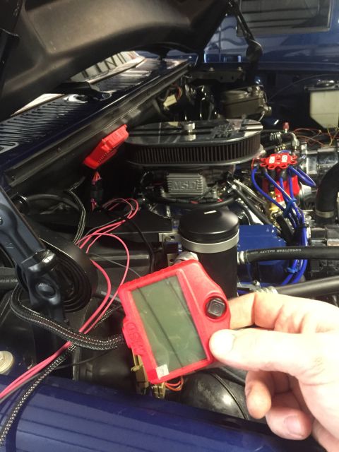 1982 Ford Bronco - A hand holds a red digital gauge in the engine bay of a blue vehicle.