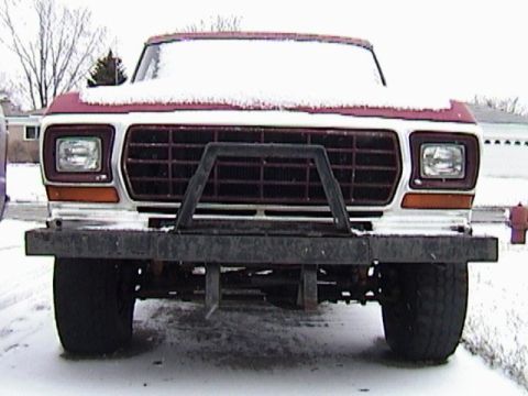 1995 Ford Bronco - Head-on view of a red-and-white late-1970s Ford truck dusted with snow, showing rectangular headlights, an amber-lensed turn signal and a h…