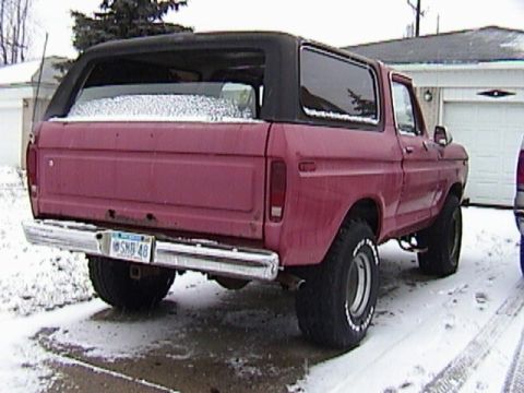 1995 Ford Bronco - Rear three-quarter view of a faded red late-1970s full-size Ford Bronco with a black removable hardtop, parked on a snowy driveway in front…