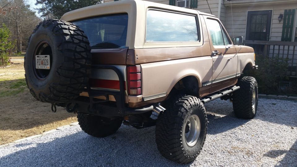 Lifted 1988 Ford Bronco, rear 3/4 view, with spare tire on back, brown exterior.