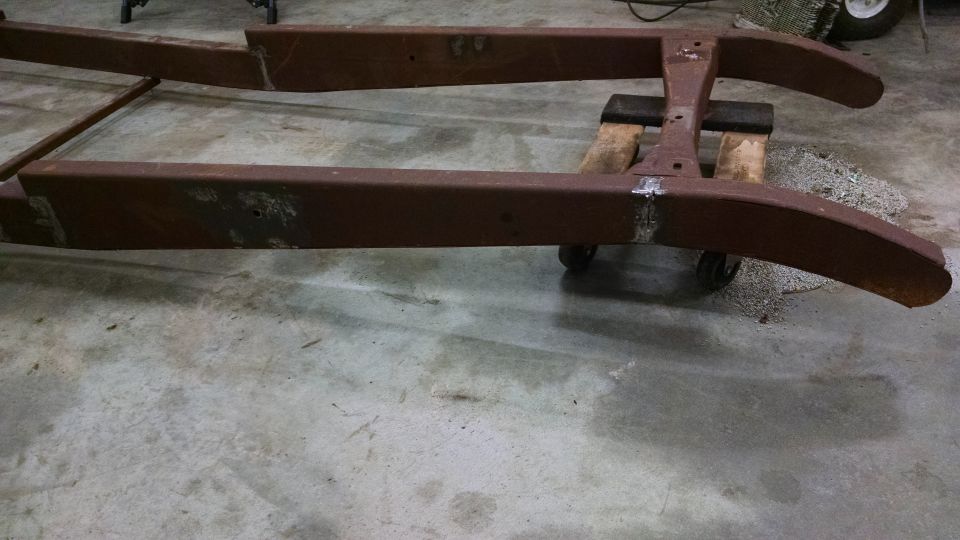 Rusty brown metal chassis frame of an old vehicle, resting on a concrete floor.