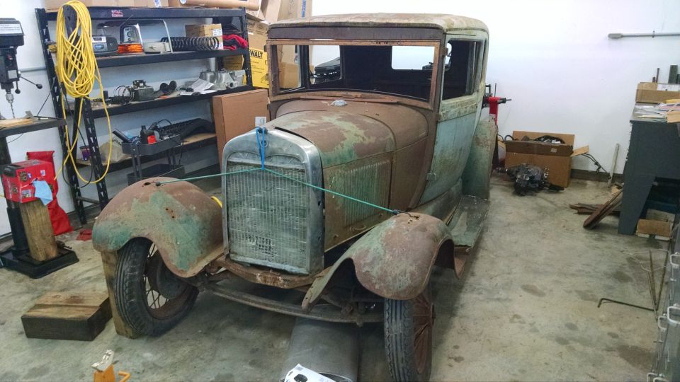 Rusty 1929 Ford Sedan in a garage, front view.