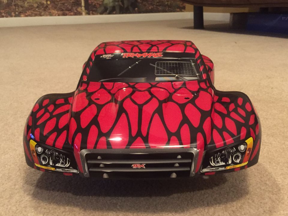Red and black patterned remote-controlled short course truck, front view, with Traxxas logo.