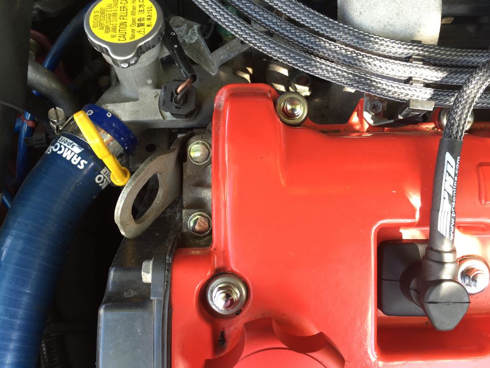 Close-up of a red engine cover with bolts, blue hose, and black wire.