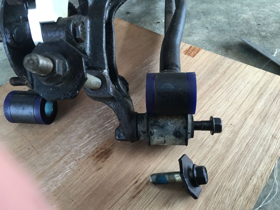 Black suspension part with blue bushings and a detached bolt on a wooden surface.