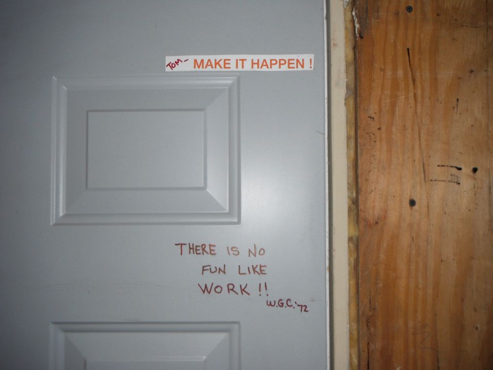Gray door with sticker and handwritten messages about work.