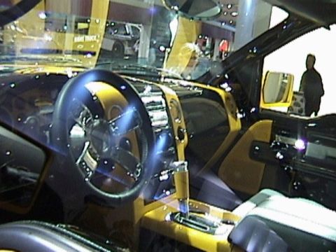 1995 Ford Bronco - The custom two-tone yellow-and-black interior of a show truck photographed through the glass at an indoor auto show, with a chrome-spoke st…