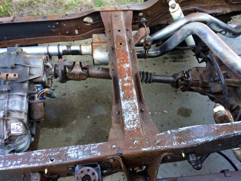 1994 Ford Bronco - The rusty frame of a 1994 Ford Bronco is shown with the transmission, driveshaft, and part of the exhaust system visible. The vehicle is on…