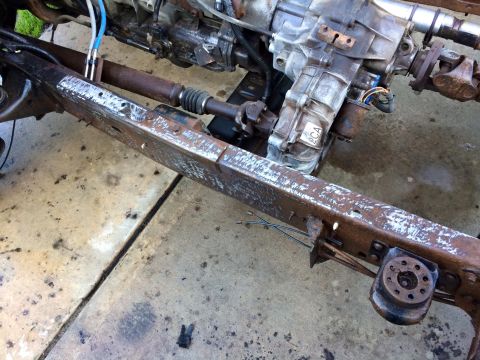1994 Ford Bronco - A close-up view of a rusty vehicle frame with a transmission and driveshaft visible. The frame appears to have been recently worked on, wit…