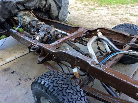 1994 Ford Bronco - The heavily rusted frame of a 1994 Ford Bronco is shown, with the transmission and drivetrain components visible. The vehicle is outdoors o…