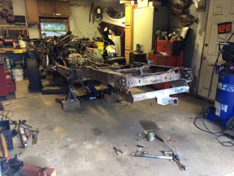 1994 Ford Bronco - The chassis and engine of a vehicle are elevated on jack stands in a garage. Various tools and equipment are scattered around the concrete…