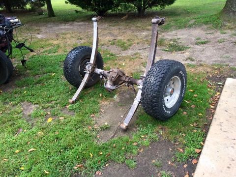 1994 Ford Bronco - A rear axle assembly with two large tires and leaf springs is shown resting on the ground outdoors. The tires are BFGoodrich All-Terrain T/…