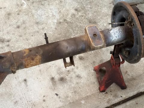 1994 Ford Bronco - A rusty rear axle assembly, likely from a 1994 Ford Bronco, is supported by a red jack stand on a concrete surface. The assembly includes a…