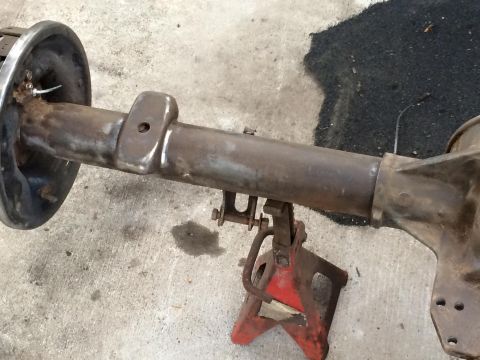1994 Ford Bronco - A rusted rear axle assembly, likely from a 1994 Ford Bronco, is supported by a red jack stand on a concrete surface.