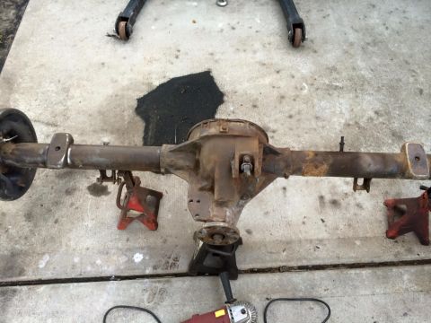 1994 Ford Bronco - A rusty rear axle assembly, likely from a 1994 Ford Bronco, is supported by jack stands on a concrete surface. A brake drum is visible on t…