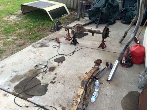 1994 Ford Bronco - A disassembled rear axle assembly for a Ford Bronco is supported by jack stands on a concrete driveway. Various automotive parts, including…