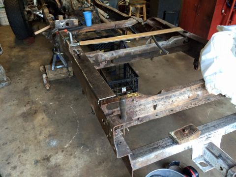 1994 Ford Bronco - The rusty frame of what appears to be a 1994 Ford Bronco is shown in a garage setting, supported by jack stands. Various tools and automoti…
