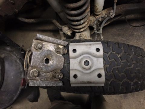 1994 Ford Bronco - Two metal spring plates are shown resting on a tire. The plate on the left is attached with bolts and nuts and appears to be a U-bolt plate…