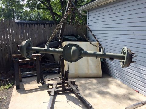 1994 Ford Bronco - A heavy-duty rear axle assembly, painted olive drab, is suspended by chains from a hoist. The axle is supported by a floor jack and stands…