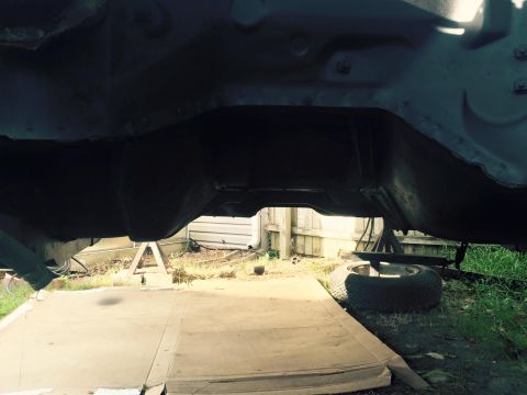 1994 Ford Bronco - The underside of a vehicle, likely a 1994 Ford Bronco, is shown supported by jack stands. A spare tire rests on the ground to the right of…