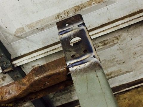 1994 Ford Bronco - A close-up view shows a rusty metal bracket attached to a section of what appears to be a vehicle frame, with a white garage door in the ba…