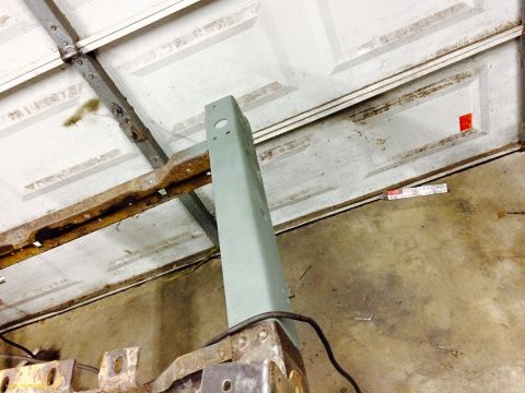 1994 Ford Bronco - A close-up, low-angle shot shows a light green metal support beam attached to a rusty metal frame, with a white garage door in the backgrou…