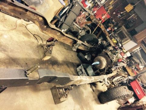 1994 Ford Bronco - A disassembled vehicle frame and engine are laid out on a concrete floor, surrounded by tools and parts. The frame appears to be from an ol…