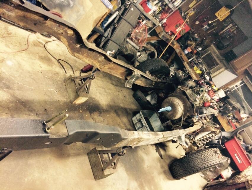 Disassembled vehicle frame and engine on concrete floor with tools and parts.