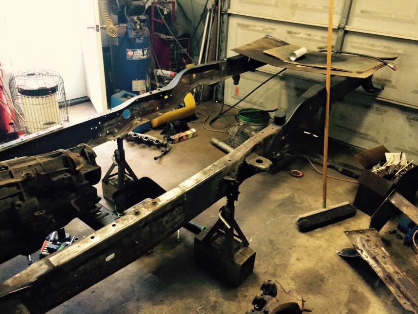 1994 Ford Bronco frame on jack stands in a garage with tools and parts.