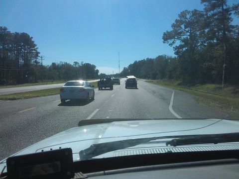 1994 Ford Bronco - A white sedan is seen from the interior of another vehicle driving on a highway. Several other vehicles are visible ahead on the road.