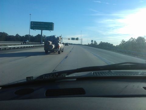 1994 Ford Bronco - A pickup truck is driving on a highway, carrying a large load of rolled-up material, possibly carpet or insulation, in its bed. The truck i…
