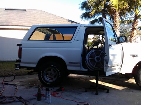 1994 Ford Bronco - The side view of a white Ford Bronco with the driver's side door open, revealing a large fan inside. The vehicle is parked on a concrete dr…