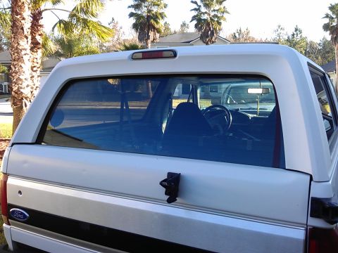 1994 Ford Bronco - The rear of a white Ford Bronco is shown with the tailgate and rear window. A black stripe runs horizontally across the tailgate, and a For…